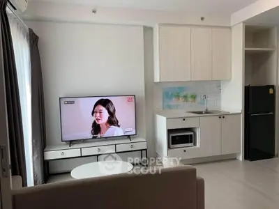 Modern living room with TV and compact kitchen in open layout apartment.