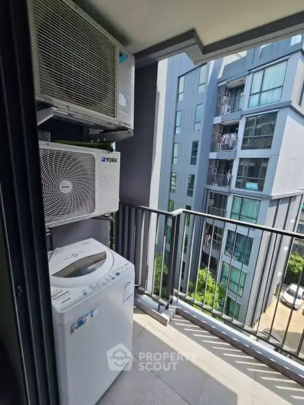 Modern apartment balcony with washing machine and air conditioning units, overlooking a contemporary building.