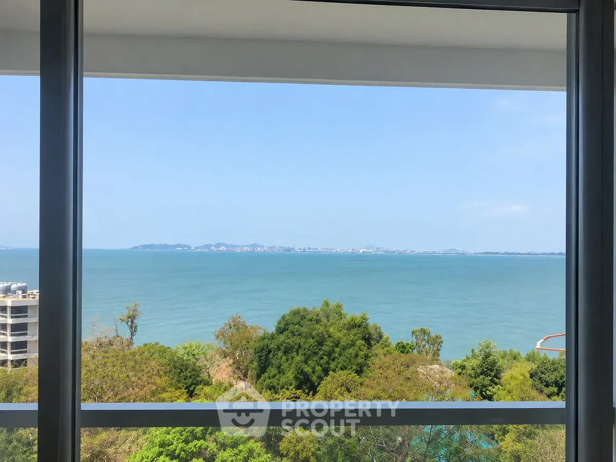 Stunning ocean view from a high-rise apartment window, showcasing serene blue waters and lush greenery.