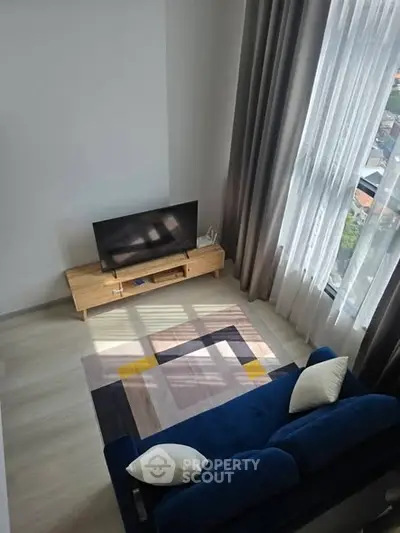 Modern living room with stylish blue sofa, wooden TV stand, and large window with city view.