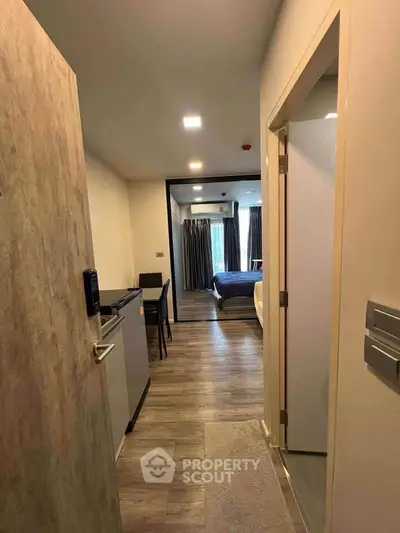 Modern apartment entrance leading to cozy bedroom with wooden flooring and natural light.