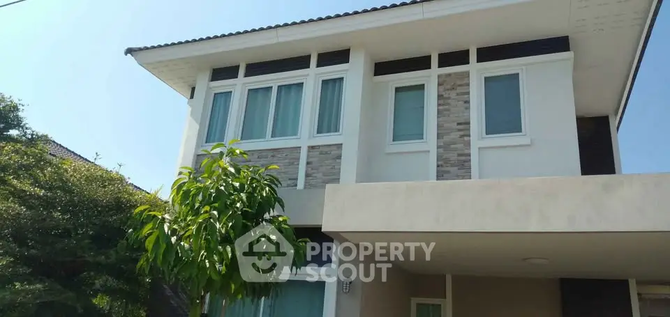 Modern two-story house with large windows and a small tree in the front yard.