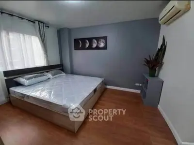 Modern bedroom with wooden flooring and moon phase artwork, featuring a comfortable bed and air conditioning.