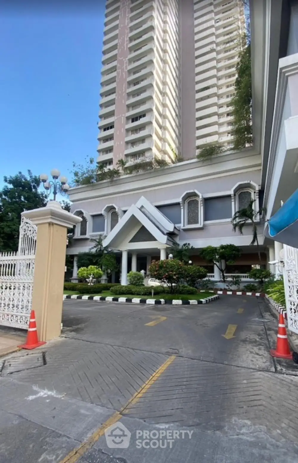 Elegant high-rise building entrance with lush landscaping and gated driveway.
