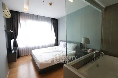 Modern bedroom with glass partition and ensuite bathtub, featuring sleek design and natural light.