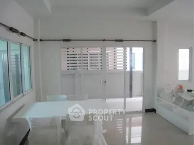 Modern dining area with sliding glass doors leading to a balcony, featuring sleek white furniture and ample natural light.