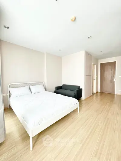 Spacious and bright bedroom with a large comfortable bed and sleek hardwood flooring, complemented by a cozy sitting area with a modern sofa.