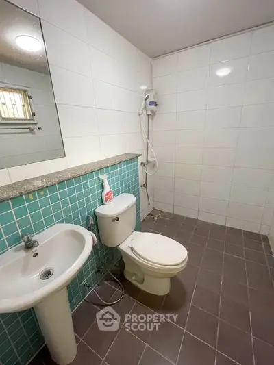 Modern bathroom with white tiles, pedestal sink, and shower area in a real estate property.