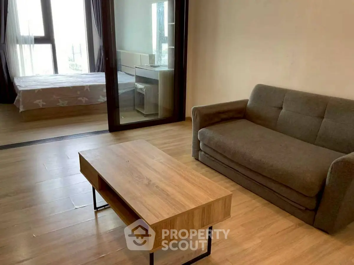 Modern studio apartment with cozy living area and bedroom, featuring wooden flooring and large windows.