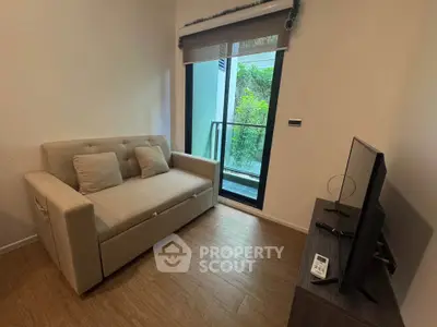 Cozy living room with sofa and TV, featuring a view of the balcony and greenery.