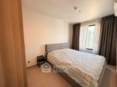 Cozy bedroom with large window and modern furnishings in a high-rise apartment.