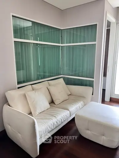 Modern living room with elegant white sofa and ottoman, featuring stylish glass panel walls.