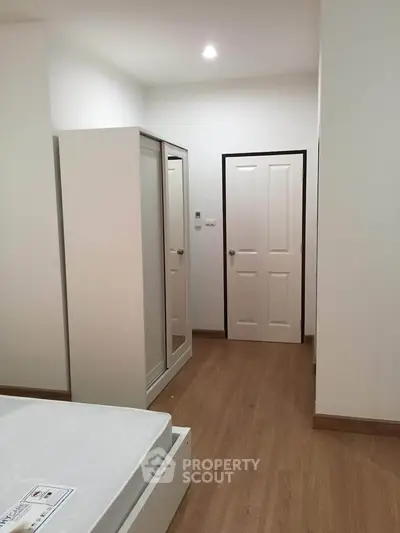 Modern bedroom with wooden flooring and white furniture, featuring a sleek wardrobe and comfortable bed.