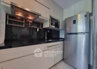 Modern kitchen with sleek cabinetry, stainless steel fridge, and built-in microwave in a compact layout.