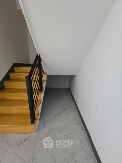 Modern staircase with sleek black railing and wooden steps in a minimalist interior design.