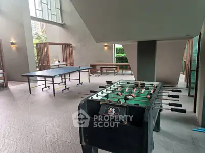Spacious recreational area with foosball and table tennis tables in modern building.