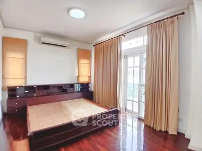 Spacious bedroom with wooden flooring and large windows for natural light.