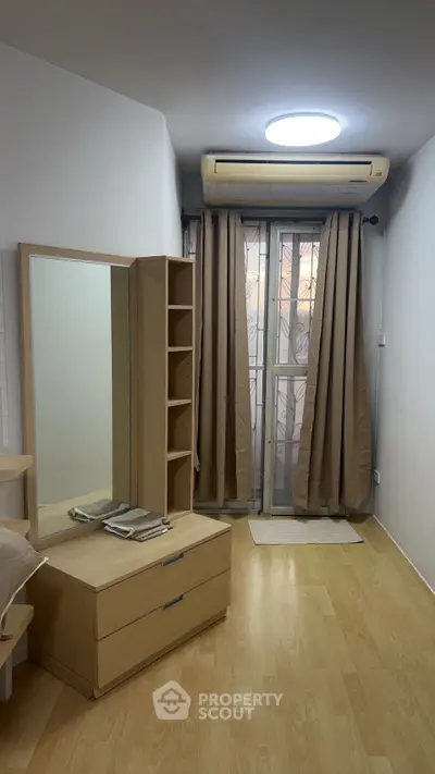 Cozy bedroom with wooden flooring, air conditioning, and ample natural light through large windows.