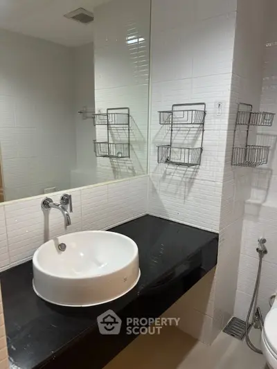 Modern bathroom with sleek black countertop and white basin, featuring wall-mounted storage baskets.