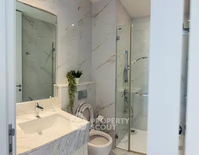 Modern bathroom with marble sink and glass shower enclosure in luxury apartment.