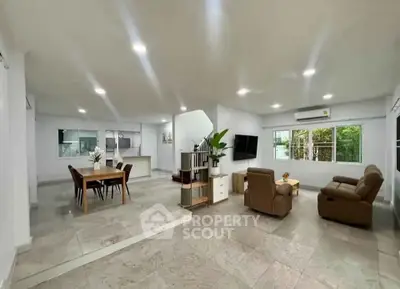 Spacious open-plan living room with modern decor and dining area, featuring large windows and stylish furniture.