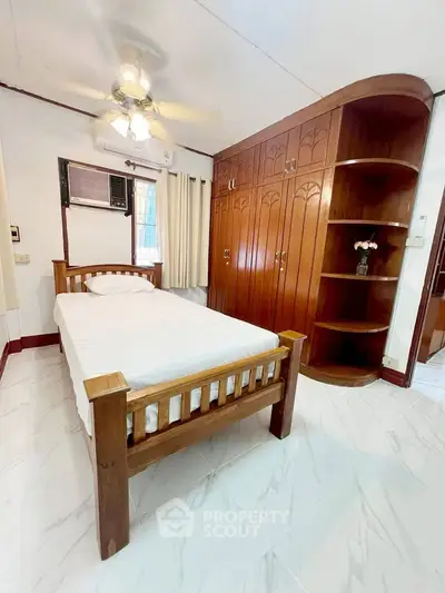 Cozy bedroom with wooden furniture and built-in wardrobe, featuring a ceiling fan and air conditioning.