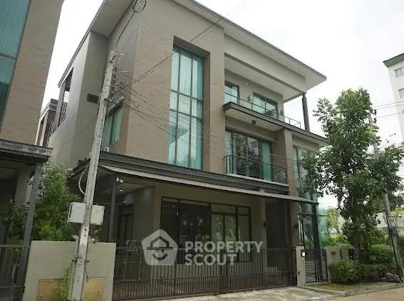 Modern three-story house with large windows and a gated entrance in a suburban neighborhood.