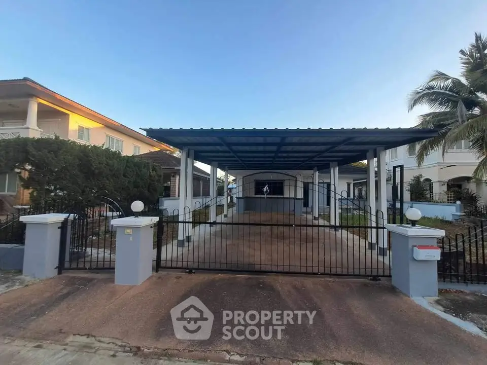 Spacious residential property with gated driveway and carport, surrounded by lush greenery and palm trees.