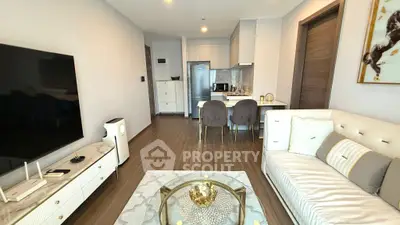 Modern living room with elegant decor and open kitchen layout, featuring a sleek TV and stylish furniture.