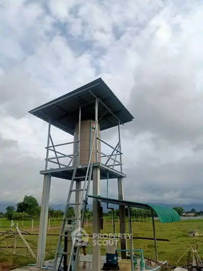Rural water tower structure with metal roof and ladder in open field setting