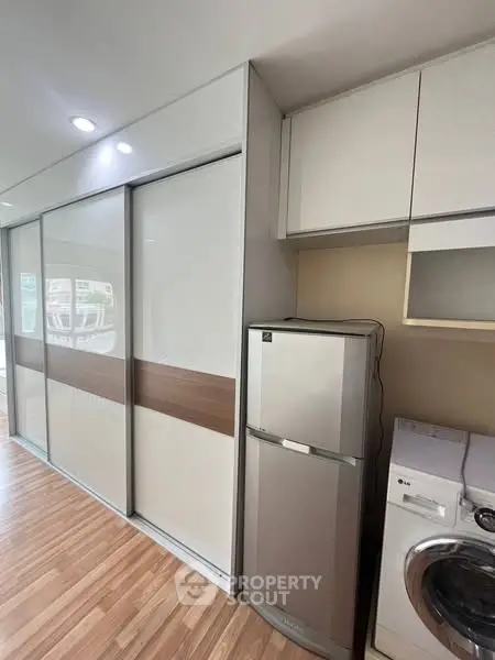 Modern apartment interior with sleek storage and appliances, featuring a fridge and washing machine.
