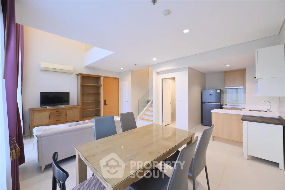 Spacious modern living room with open kitchen and dining area, featuring stylish furniture and ample natural light.