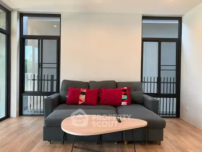 Modern living room with stylish sofa and wooden coffee table, featuring large windows for natural light.
