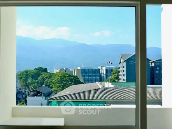 Stunning mountain view from a modern apartment window, showcasing urban landscape and lush greenery.