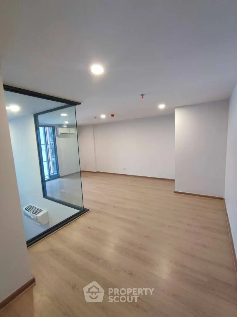 Spacious modern living room with wooden flooring and large glass partition, perfect for contemporary urban living.