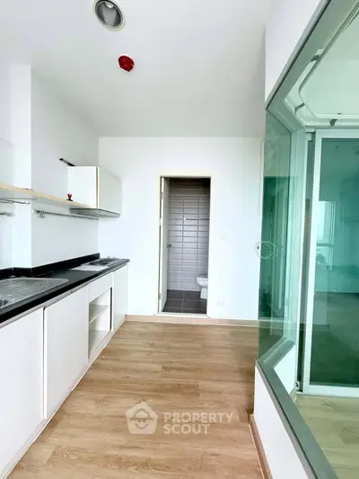 Modern kitchen with sleek cabinetry and open layout, featuring a view into a bright adjacent room.