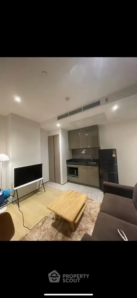 Modern living room with compact kitchen, sleek furniture, and ambient lighting in a cozy apartment.