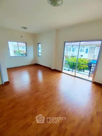 Spacious room with wooden flooring and large windows offering natural light and balcony access.