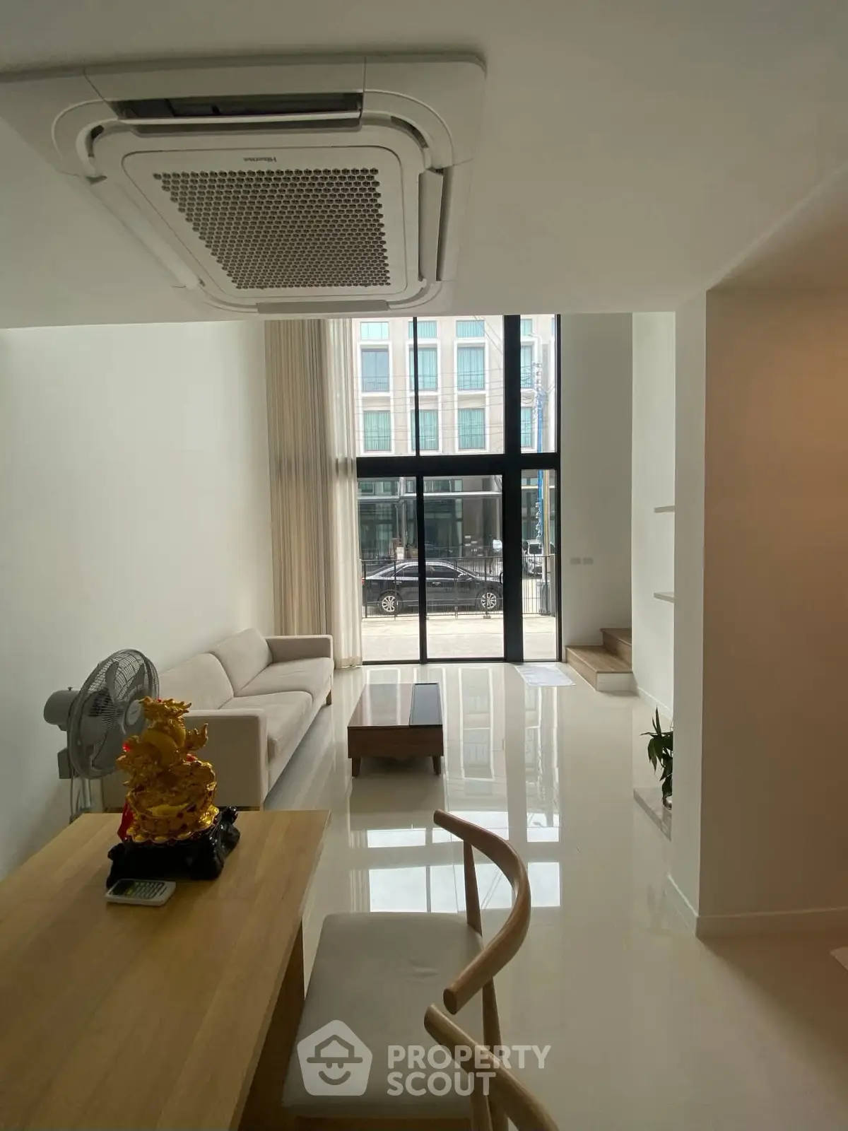 Modern living room with high ceiling and large windows, featuring minimalist furniture and bright natural light.