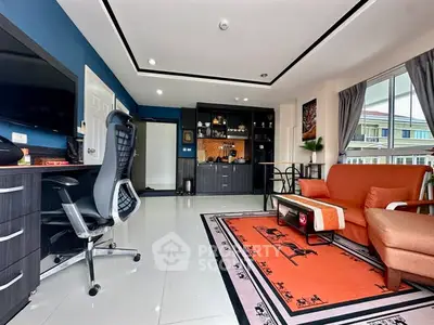 Modern living room with stylish decor and office setup, featuring a vibrant orange sofa and sleek black furniture.