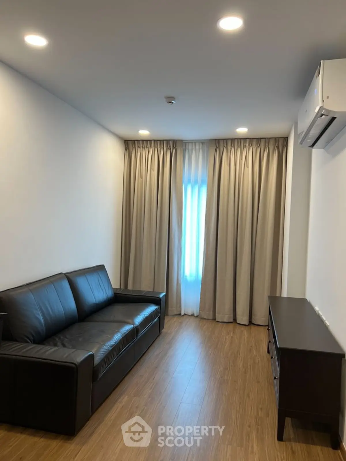 Modern living room with sleek black sofa, wooden flooring, and elegant curtains.