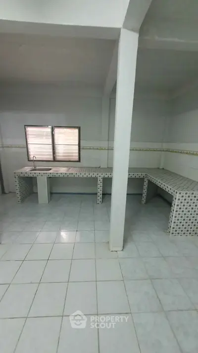 Spacious tiled room with built-in counters and natural light, ideal for versatile use.