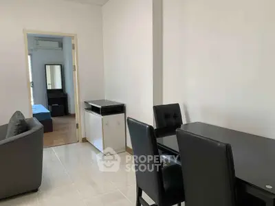 Modern apartment interior with dining area and view into bedroom, featuring sleek black furniture.