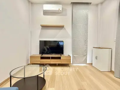 Modern living room with sleek furniture and wooden flooring, featuring a mounted TV and air conditioning.