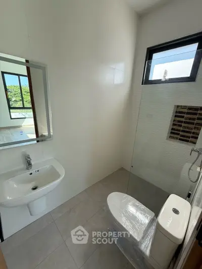 Modern bathroom with sleek fixtures and natural light, featuring a glass shower enclosure and stylish tile work.