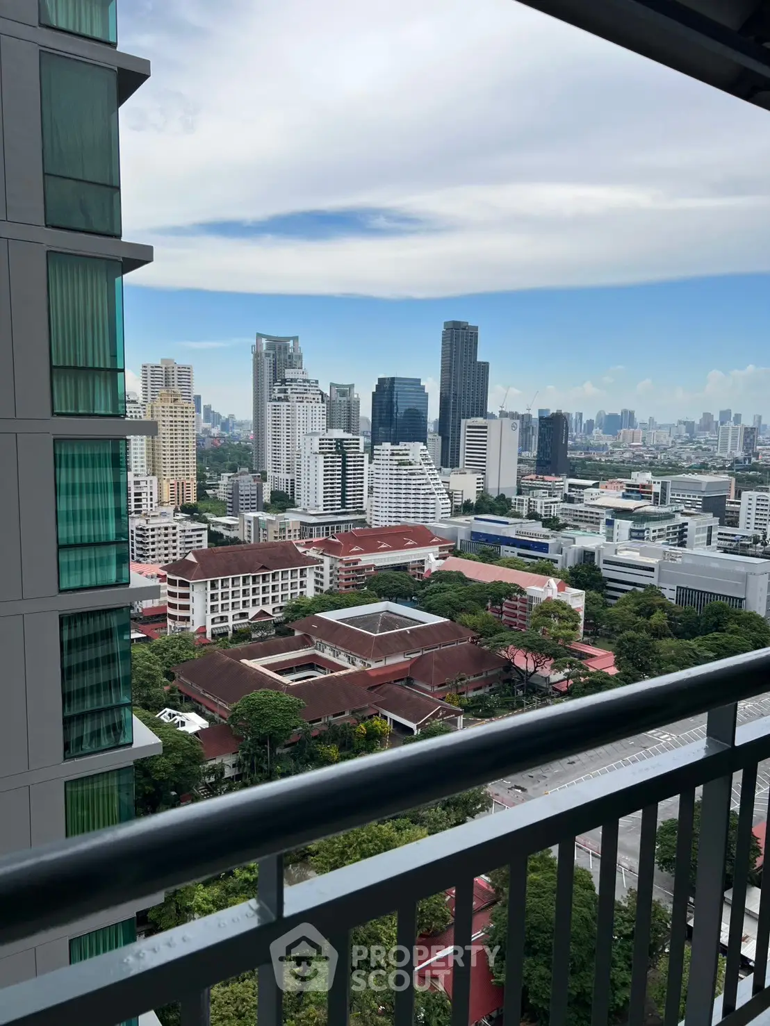 Stunning cityscape view from a high-rise balcony overlooking urban skyline and lush greenery.