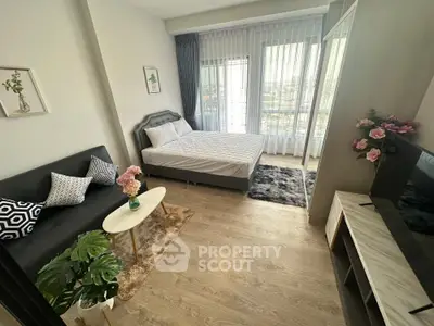 Modern studio apartment with stylish decor, featuring a cozy bed, sofa, and large window for natural light.