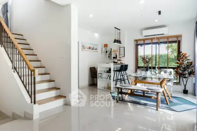 Modern open-plan living room with dining area and staircase, featuring sleek design and natural light.