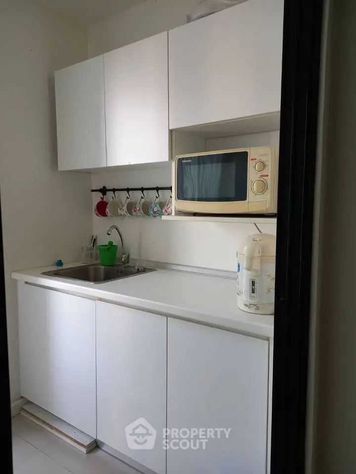 Compact kitchen with white cabinets and microwave, ideal for small apartments.