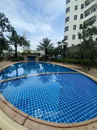 Luxurious residential pool with palm trees and modern building backdrop.